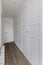 Hallway in Empty room with built-in wardrobes with white wooden doors with gold handles, matching baseboards and wooden floor
