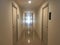 Hallway inside condo with nature lighting through window and bulb lighting with exit sign reflection on the floor.