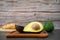 halved avocado on wooden plate and croissant on a black background