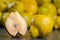 Halved and bisected quince fruit and whole fruit with pile of other quinces in blurred background