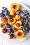 Halved peaches, nectarines, grapes, figs on white plate on white tablecloth, closeup view, top down