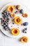 Halved peaches, nectarines, grapes, figs on white plate on white tablecloth. Vertical image