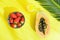 Halved Ripe Papaya Fresh Strawberries in Bowl Pineapple Juice in Tall Glass with Straw Palm Leaf on Yellow Background