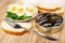 Halves of eggs and parsley in saucer, slices of bread, opened jar with sprats, fork on wooden table