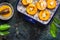 Halves of peaches with cheese and honey in baking dish on dark rustic background, top view.