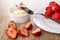 Halves of strawberries, berry on fork above bowl with condensed milk, plate with strawberry on table