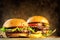 Hamburger and Double Cheeseburger with french fries rotated on wooden table background. Cheeseburgers on fresh buns