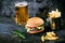 Hamburger with french fries, beer on a burnt, black wooden table. Fast food meal. Homemade hamburger consist of beef meat, lettuce