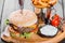 Hamburger with fresh vegetables, cheese, sauce and fries on cutting board