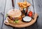 Hamburger with fresh vegetables, cheese, sauce and fries on cutting board on dark wooden background.