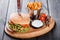 Hamburger with fresh vegetables, cheese, sauce and fries on cutting board on dark wooden background. Burger with knife.