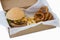 Hamburger, onion ring and french fries in a take away container on table