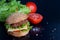 Hamburger with salad, tomato, meat on black backdrop