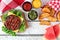 Hamburger, watermelon and potato wedges, picnic scene on white wood