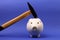 Hammer is raised above a upside down white pink piggy bank on blue background