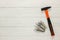 Hammer with a rubberized orange and black handle and stack of dowel nails on white wooden background