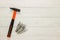 Hammer with a rubberized orange and black handle and stack of dowel nails on white wooden background. Copy space