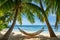 A hammock is suspended between two palm trees on a sandy beach, inviting relaxation and comfort, An inviting hammock for two