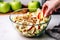 hand adding sliced almonds to a bowl of apple salad