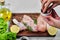 Hand adds spices to wooden plate of raw chicken meats on white background