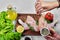 Hand adds spices to wooden plate of raw chicken meats on white background