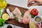 Hand adds spices to wooden plate of raw chicken meats on white background