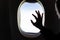 Hand on airplane window with aerial view of white clouds with silhouette man face look outside