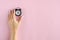 Hand with analog alarm clock composition on pink background