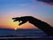 A hand and an arm as a black silhouette bends high against the still blue evening sky over the sun