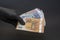 A hand in a black medical glove holds a wad of euros on a dark background, selective focus, close-up. Concept: cash payment during