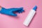 Hand in blue disposable glove reaching for surface disinfectant or hand sanitizer on pink background