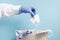 A hand in a blue disposable medical glove throws a used protective face mask into a trash can, blue background