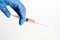Hand in blue glove holding syringe with droplet of vaccine on needle tip