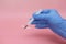 A hand in a blue glove holds a syringe. Pink background