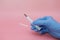 A hand in a blue glove holds a syringe. Pink background