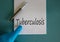 Hand in blue glove, pen, white note with word `tuberculosis`. Medical concept