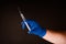 Hand in blue glove with syringe, dark background