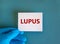 Hand in blue glove with white card. Concept word `lupus`. Medical concept. Copy space, beautiful blue background