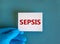 Hand in blue glove with white card. Concept word `sepsis`. Medical concept. Copy space, beautiful blue background