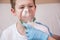 A hand in a blue medical glove holds a breathing mask for a boy in a white t-shirt. medical procedures at home