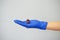 A hand in a blue medical glove holds a virus figurine on a gray background