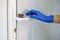 A hand in a blue medical glove reaches for a door handle with viruses