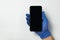 Hand in blue nitrile gloves holding smartphone on white background. Blank black screen. Copy space. Mock up