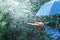 Hand and blue umbrella under heavy rain against nature background. Rainy weather concept