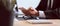 Hand of businessman in a black suit using smartphone on wooden table with typing message to contact customer and eye glasses.