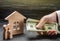 The hand of a businessman stretches a wad of money to the family figures near the wooden house. Providing a mortgage loan