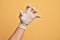 Hand of caucasian young man with medical glove over isolated yellow background grasping aggressive and scary with fingers,