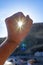 hand closed fist making a circle pointing to the sun, the light piercing, under a blurred beach background.