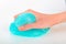 Hand clutching a light turquoise slime on light background.Close up.Soft focus.Concept of gaming, children`s entertainment,