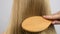 Hand is combing healthy long straight hair with wooden hairbrush. Haircare. Beautiful and smooth blonde hair